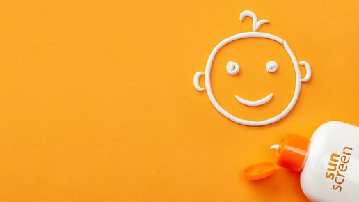 smiley face drawn by suncream on orange background next to sunscreen bottle with cap open