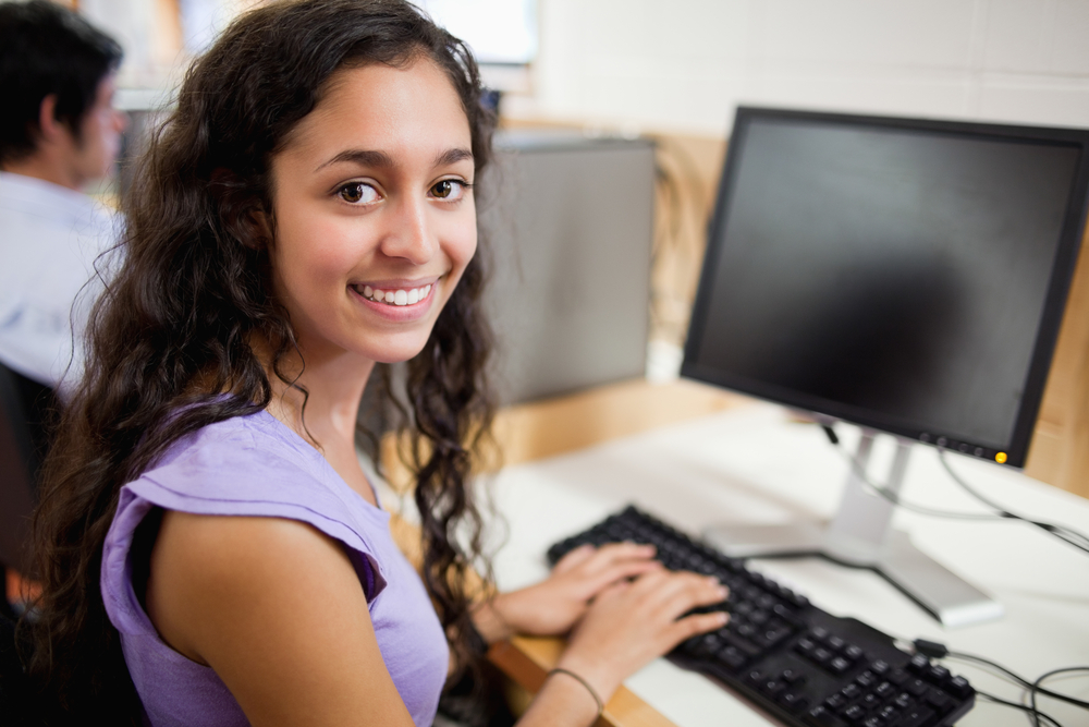 Smiling brunette student posing with a computer in an IT room