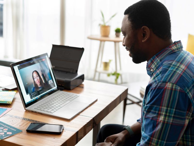 A man sits at a table, having a video call with a woman