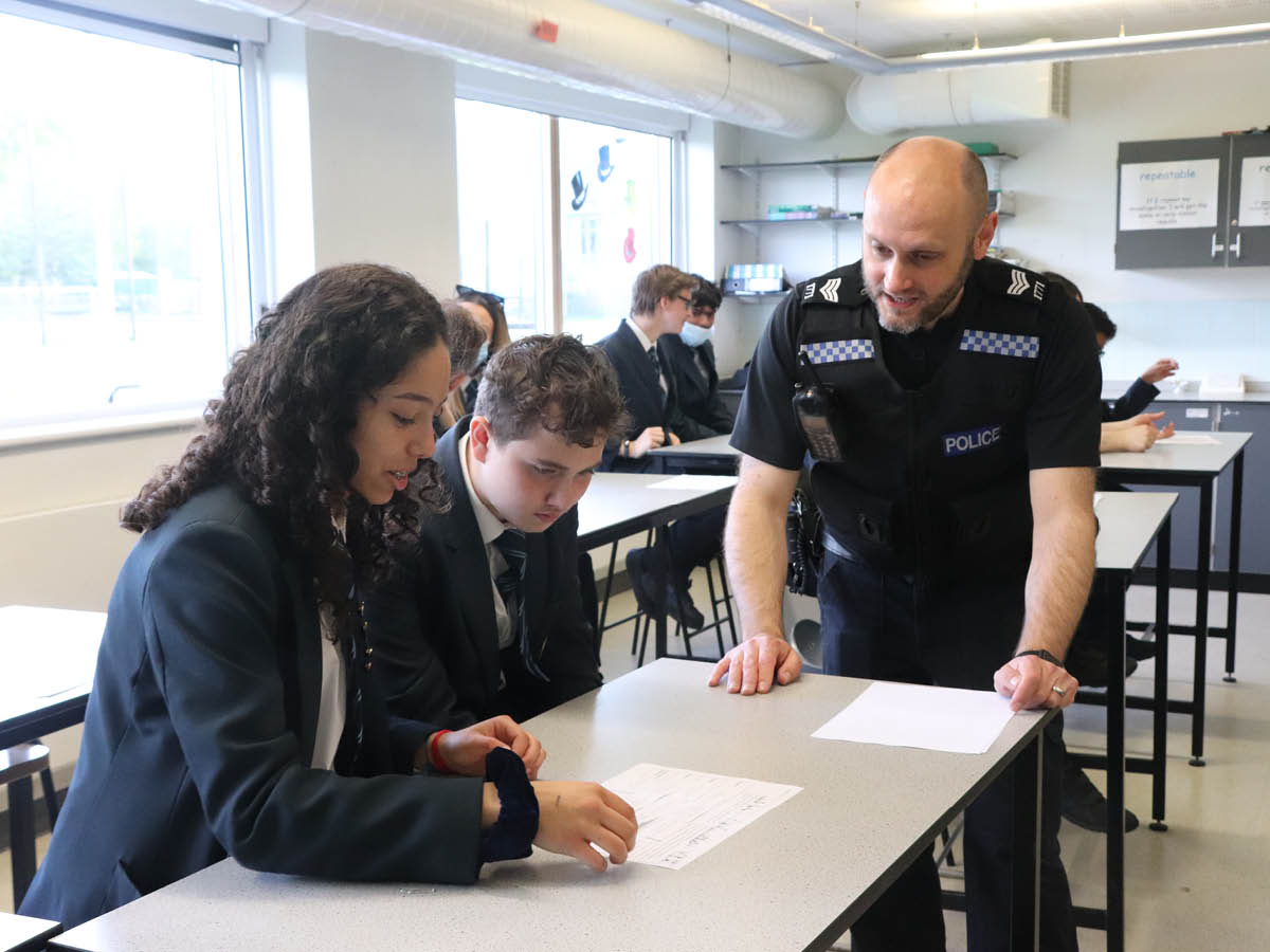 Police officer helping pupil in classroom